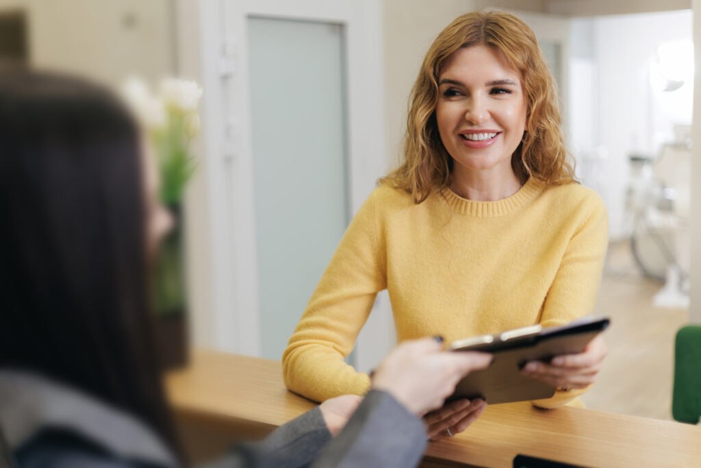 Smiling caucasian female adult with folder for papers at reception desk of clinic.